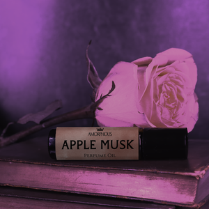 Amorphous Apple Musk perfume oil with a pink rose on an old book against a purple background