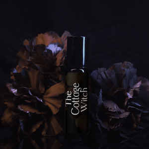 Black bottle labeled 'The Cottage Witch' with decorative flowers on a dark background