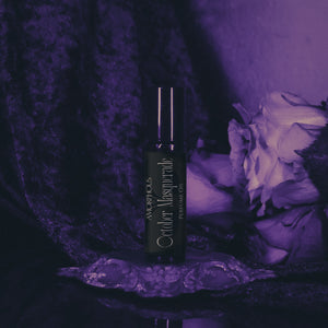 Black bottle labeled 'October Masquerade' on a stand with flowers in a purple-lit setting